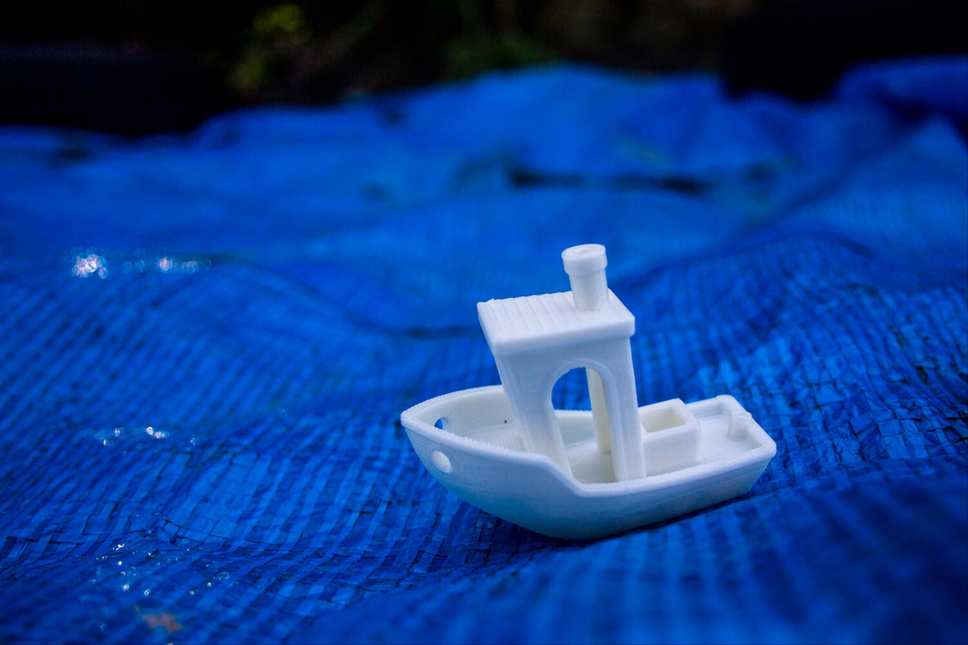 A small plastic boat that is 'sailing' on a blue tarpaulin