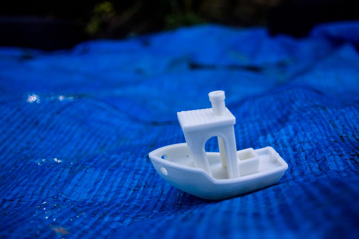 A small plastic boat that is 'sailing' on a blue tarpaulin